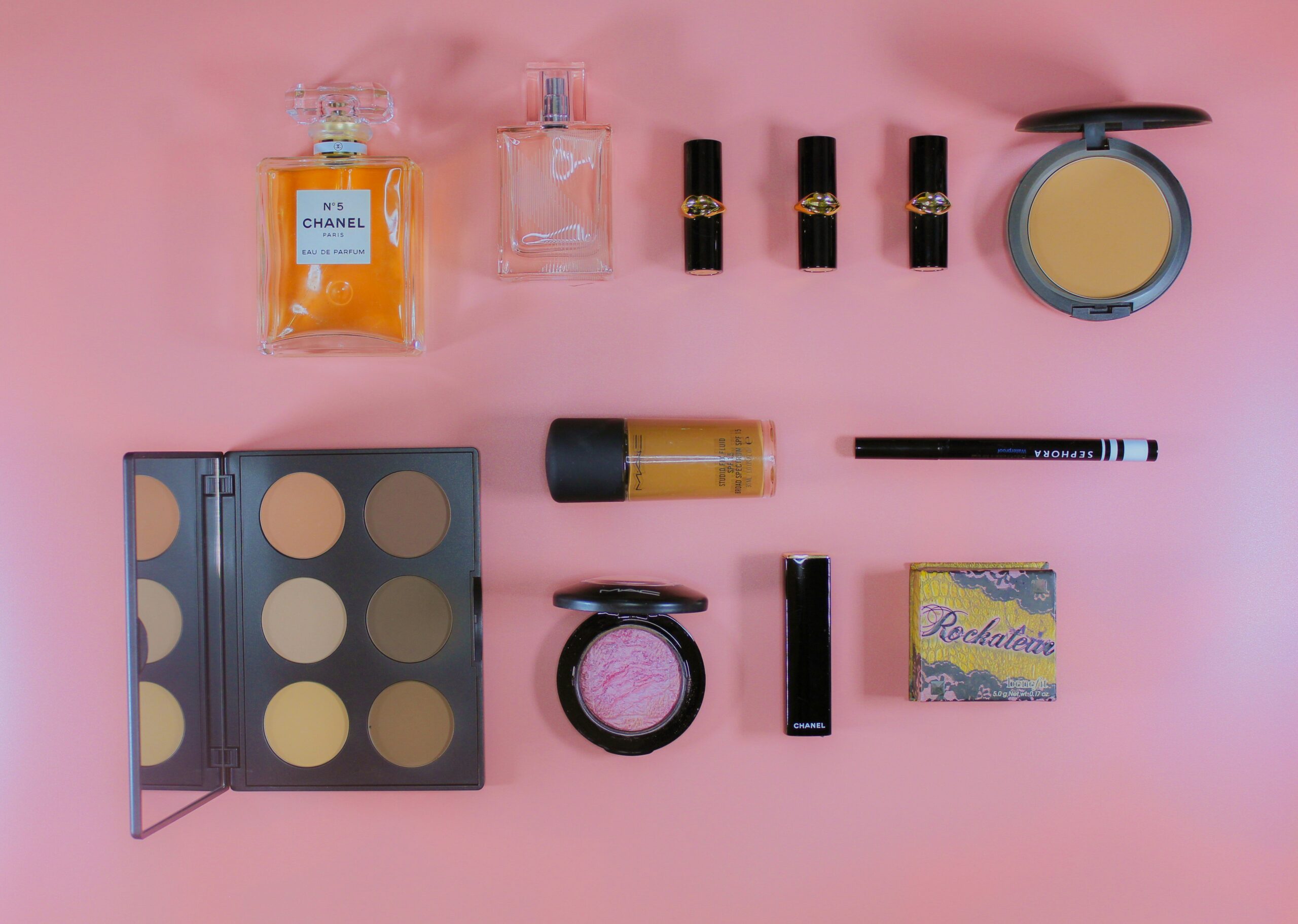 A flat-lay photo featuring various wedding makeup essentials, including foundation bottles, brushes, and lipsticks