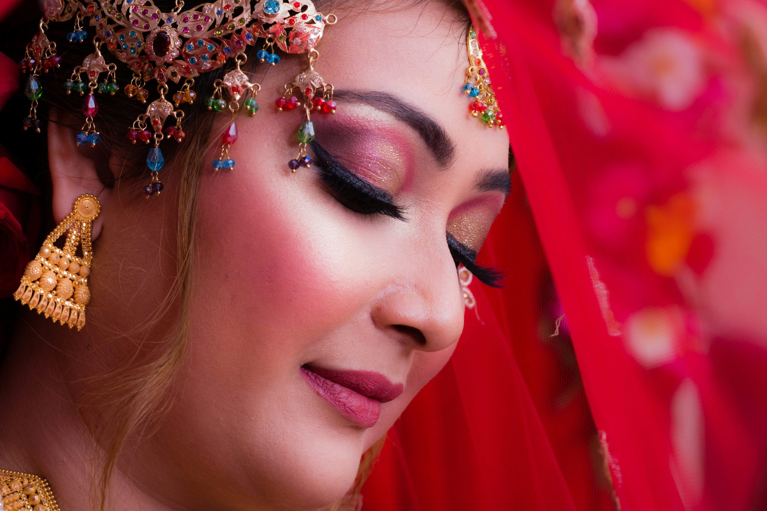 Image of a smiling bride with flawless makeup sitting elegantly against a floral backdrop.