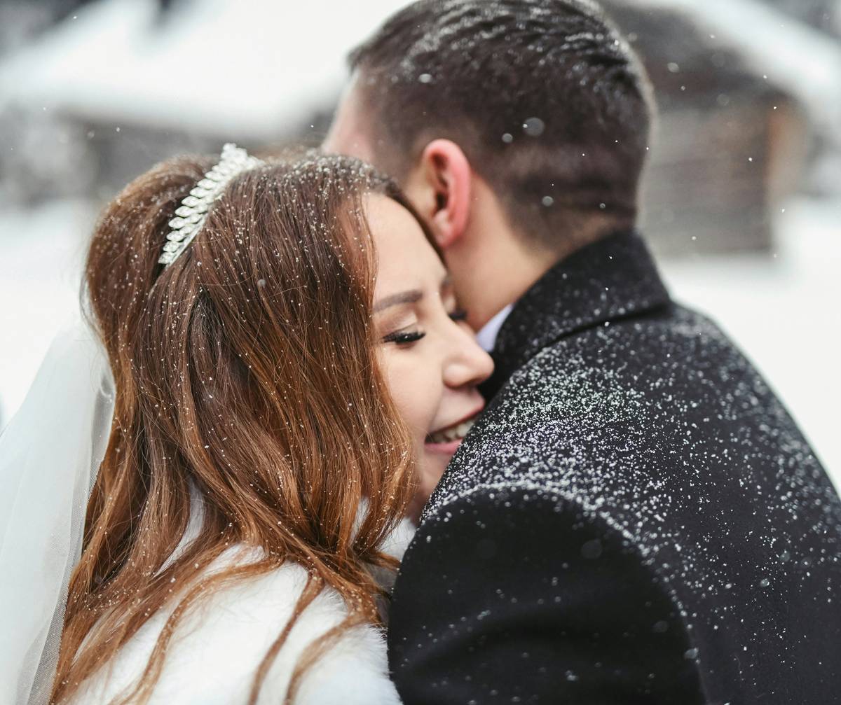 Professional makeup artist applying blush on a bride in front of a snowy window.