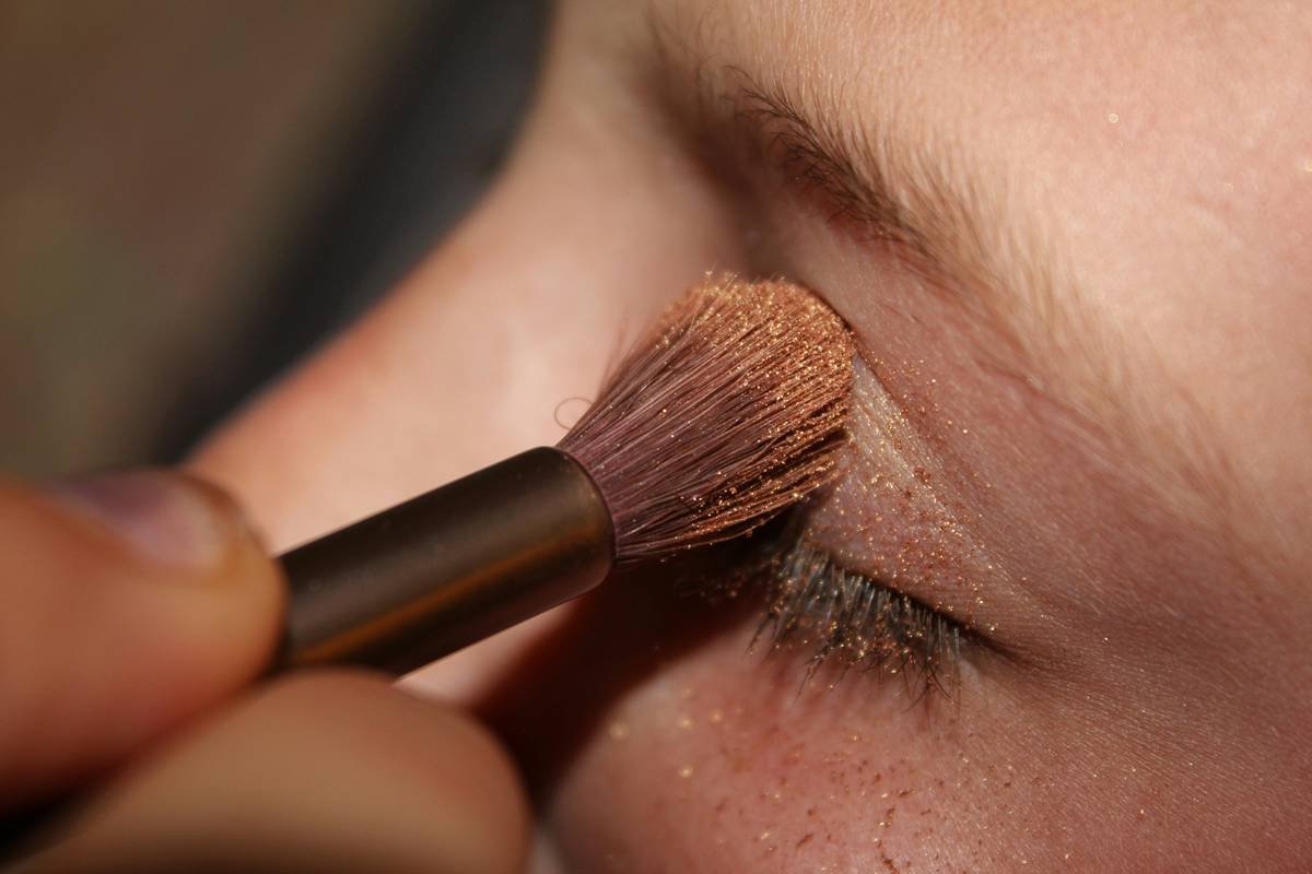 Side-by-side comparison showing how the same makeup looks under natural daylight vs. flash photography—highlighting how shimmer and dark liner appear exaggerated in photos